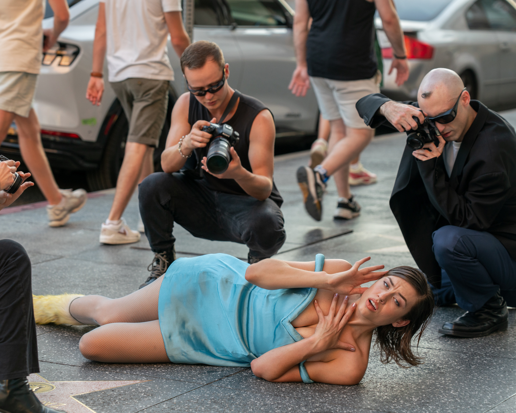 Model in a blue dress on the ground of hollywood bouevard chased by paparazzi